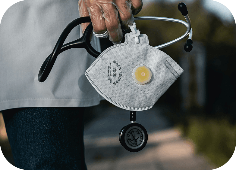 Mão de um médico de jaleco segurando um estetoscópio e uma máscara PFF2